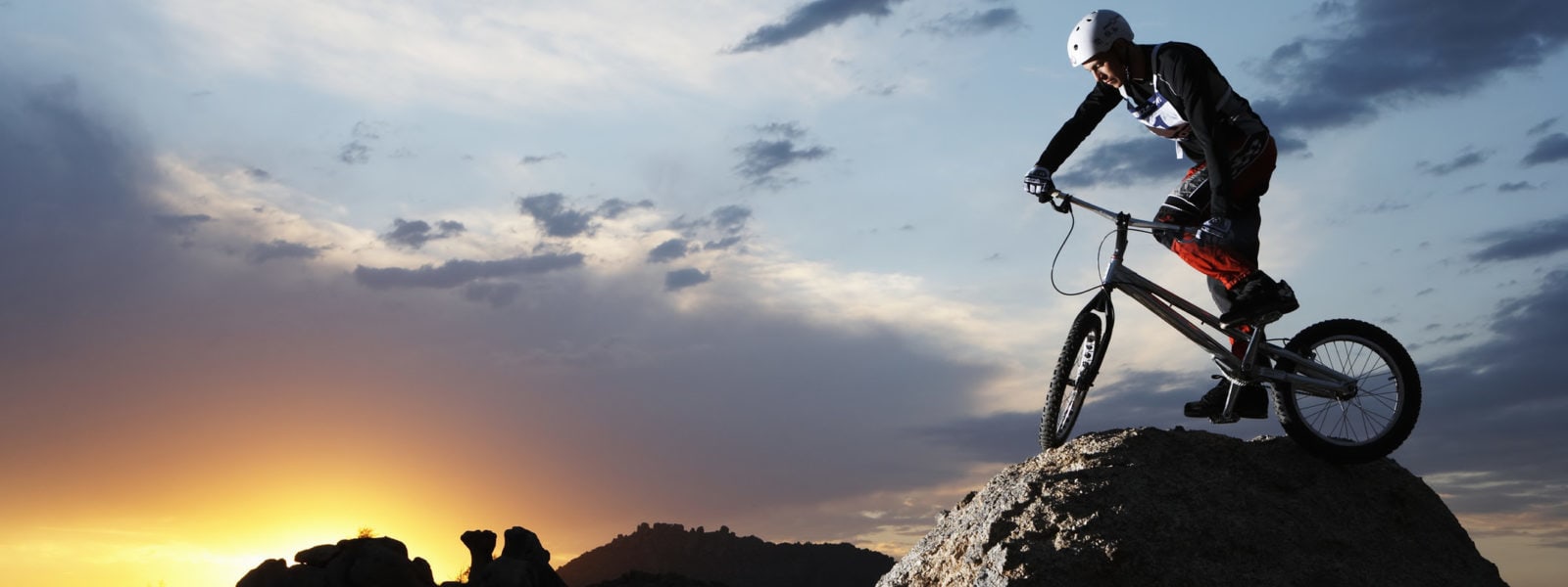 Bike rider balancing on rock boulder, side view