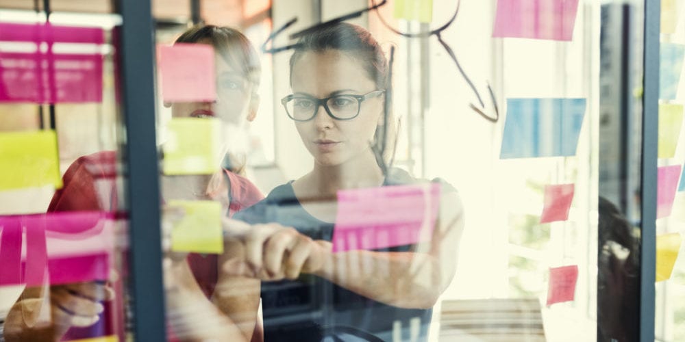 Two business women working together on wall glass